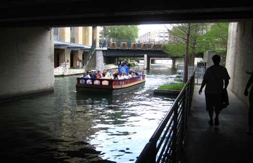 Walking the San Antonio Riverwalk with a river barg passing by.