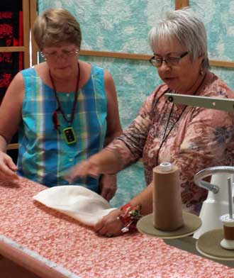 Yvonne is helping Gwen quilt a blanket with the Jojoba Hills long arm quilt machine, Behind: a view of the machine