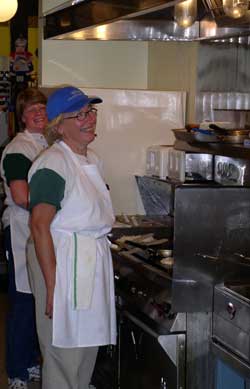 Gwen is behind Claudia, the cook, standing at the grill.